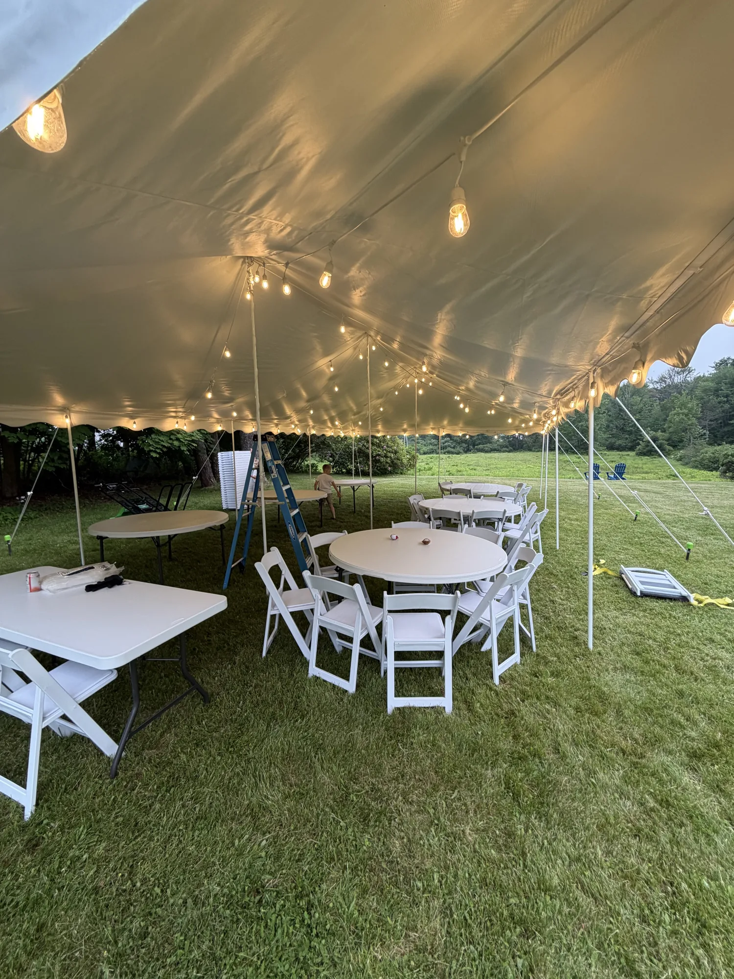 Tented fundraiser-style dinner setup with tables, chairs, and string lights